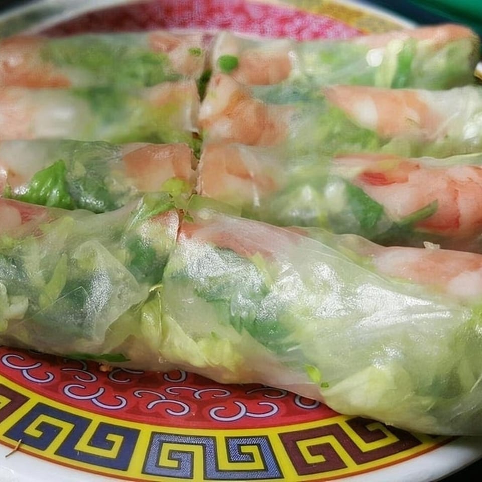 Close-up of fresh Vietnamese spring rolls with shrimp and greens on a decorative red and yellow plate.