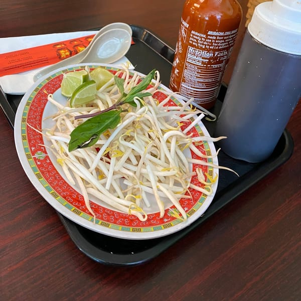A plate of bean sprouts, lime wedges, and basil, with Sriracha and hoisin sauce bottles.